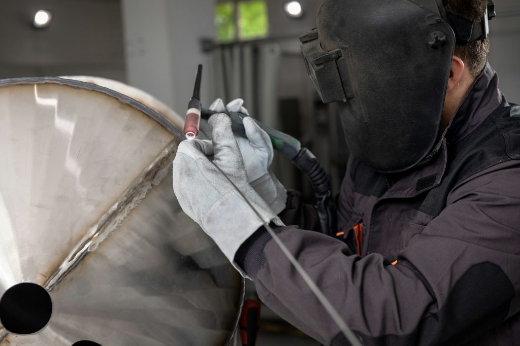 Close up of industrial worker hands welding metal structure at workshop.
